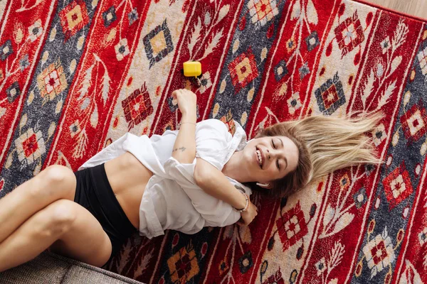 Молодая женщина слушает музыку, лежащую дома на ковре — стоковое фото