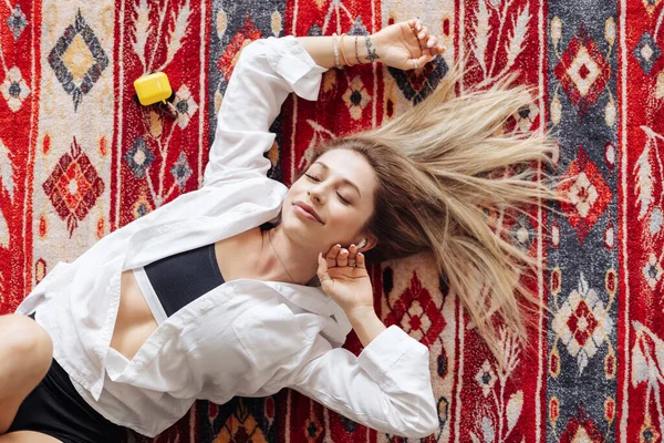 Jeune femme écoutant de la musique allongée sur le tapis à la maison — Photo