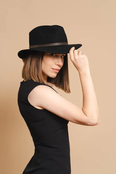 Mulher de chapéu preto e vestido, retrato em fundo bege — Fotografia de Stock