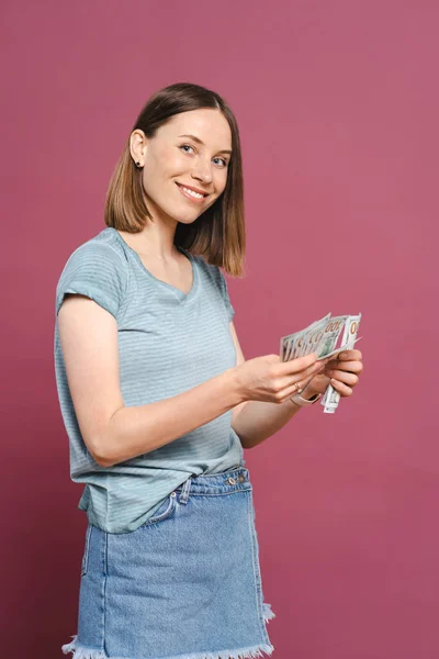 Young woman counting money on pink background — Stock Photo, Image