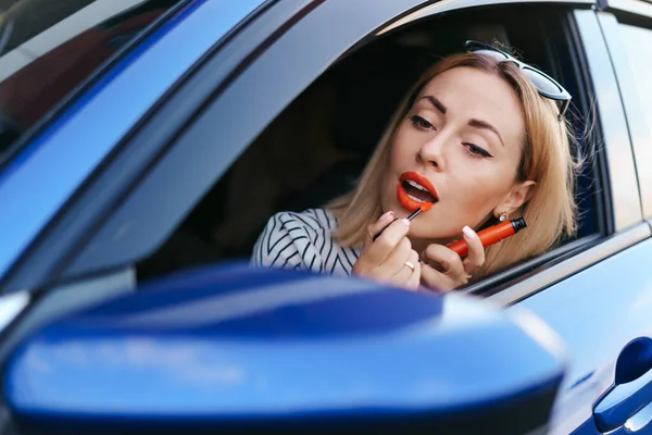 Egy nő belenéz az autó oldalsó tükrébe és kirúzsozza magát. — Stock Fotó