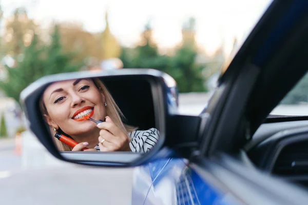 Žena při pohledu do auta boční zrcátko a uvedení na rtěnku — Stock fotografie