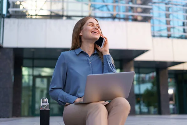 Mujer hablando por teléfono móvil y trabajando con su portátil mientras está sentada en los escalones — Foto de Stock
