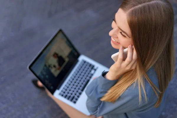 Mulher falando no celular e trabalhando com seu laptop enquanto está sentado nos passos — Fotografia de Stock