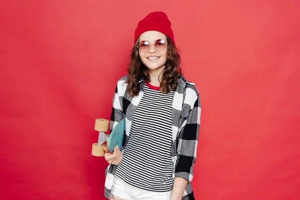 Belle adolescente posant avec penny board sur fond rouge — Photo