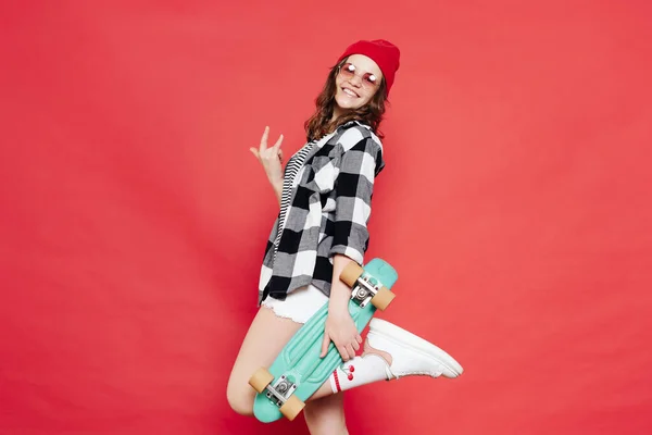 Belle adolescente posant avec penny board sur fond rouge — Photo