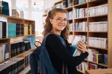 Genç kız kütüphanede kitap seçiyor.