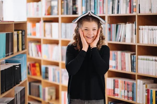 En tonårstjej håller en bok som ett tak över huvudet bland andra böcker — Stockfoto