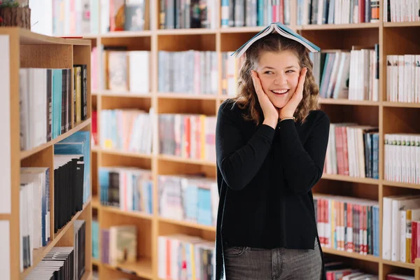 Девочка-подросток держит книгу, как крышу над головой, среди других книг — стоковое фото
