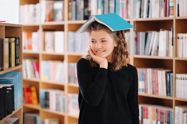 En tonårstjej håller en bok som ett tak över huvudet bland andra böcker — Stockfoto