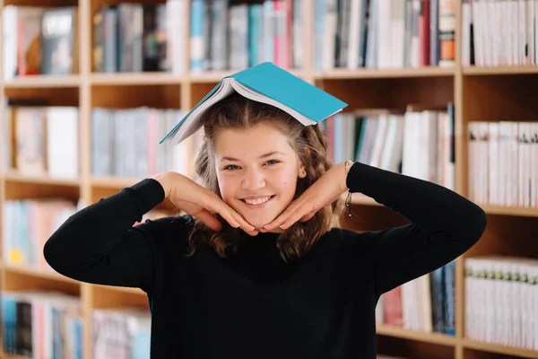 Una adolescente sostiene un libro como un techo sobre su cabeza entre otros libros —  Fotos de Stock