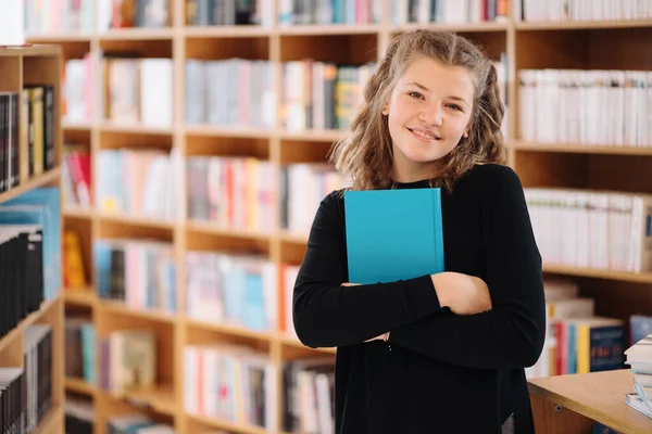 Tonårstjej som håller i en bok bland många böcker — Stockfoto