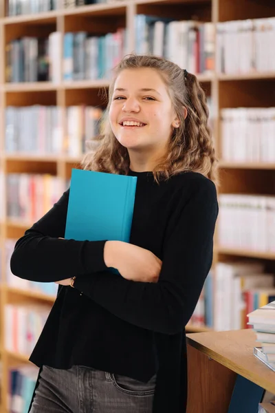 Tonårstjej som håller i en bok bland många böcker — Stockfoto
