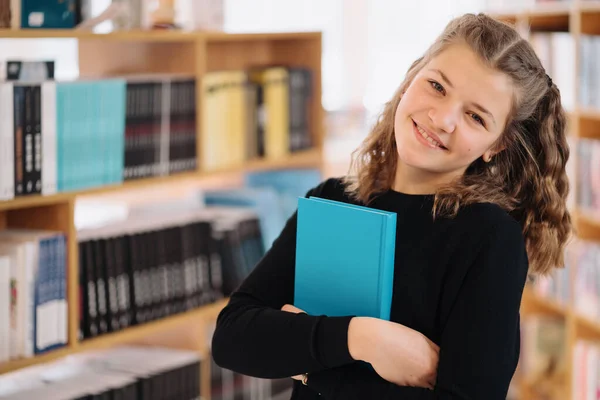 Девочка-подросток держит книгу среди множества книг — стоковое фото