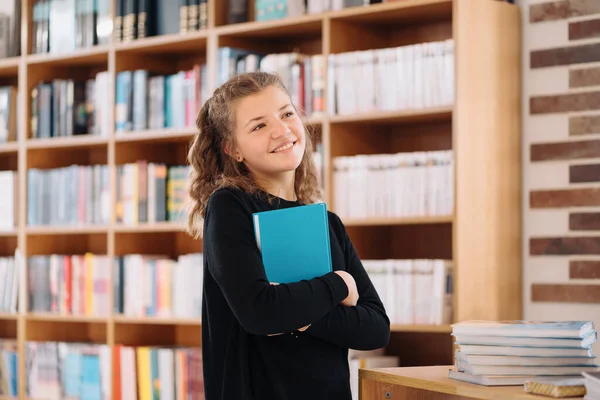 Teenager girl holding a book among many books — Stock Photo, Image