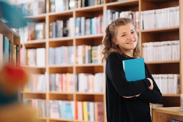 Tonårstjej som håller i en bok bland många böcker — Stockfoto