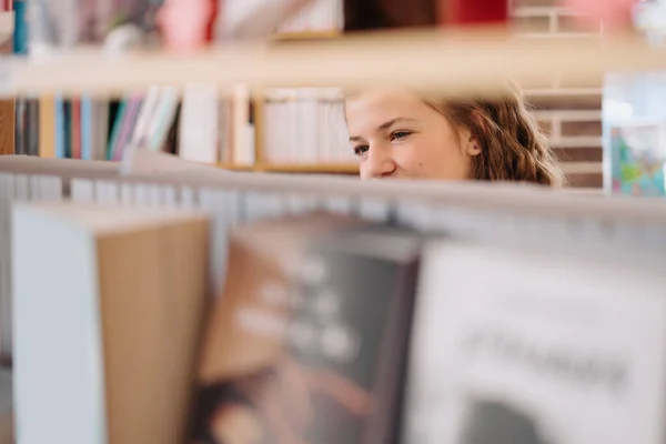 Tonårstjej plockar en bok på en bibliotekshylla — Stockfoto