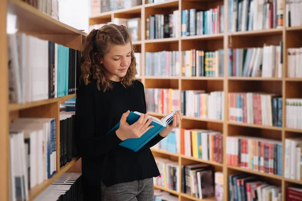 Όμορφη κοπέλα σπουδάζει διαβάζοντας ένα βιβλίο, ενώ στέκεται στο πάτωμα ανάμεσα στα βιβλία στο βιβλιοπωλείο — Φωτογραφία Αρχείου
