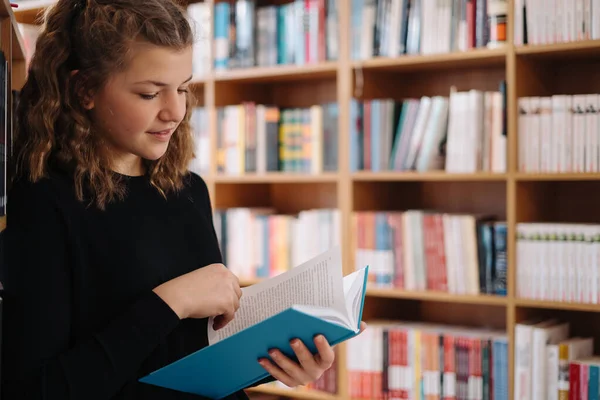 Vacker flicka studerar att läsa en bok när hon står på golvet bland böcker i bokhandeln — Stockfoto