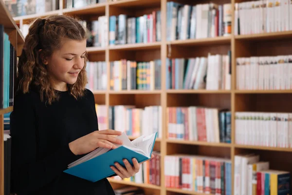 Девочка учится читать книгу, стоя на полу среди книг в книжном магазине — стоковое фото