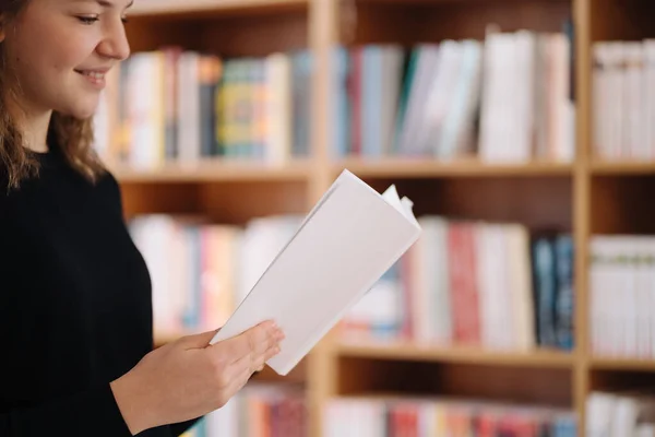 Vacker flicka studerar att läsa en bok när hon står på golvet bland böcker i bokhandeln — Stockfoto