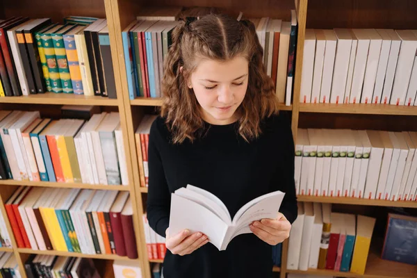 Девочка учится читать книгу, стоя на полу среди книг в книжном магазине — стоковое фото