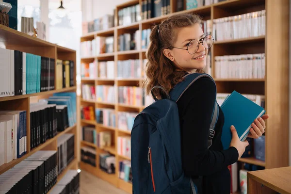 Tonårstjej plockar en bok i biblioteket — Stockfoto