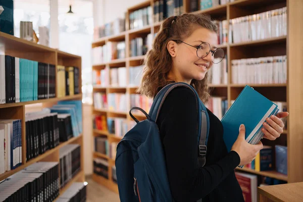 Tonårstjej plockar en bok i biblioteket — Stockfoto