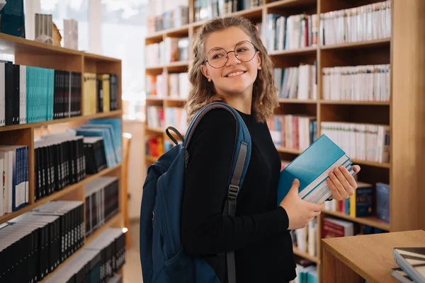 Tonårstjej plockar en bok i biblioteket — Stockfoto