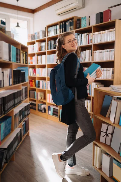 Tonårstjej plockar en bok i biblioteket — Stockfoto