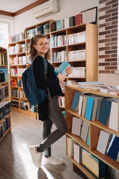 Μια έφηβη διαλέγει ένα βιβλίο στη βιβλιοθήκη. — Φωτογραφία Αρχείου
