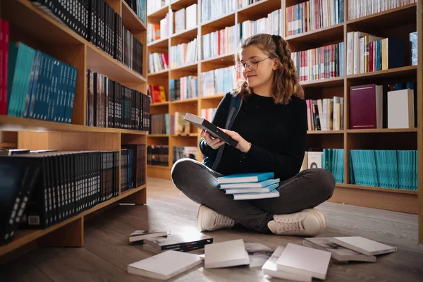 Vacker flicka studerar att läsa en bok medan hon sitter på golvet bland böcker i bokhandeln — Stockfoto