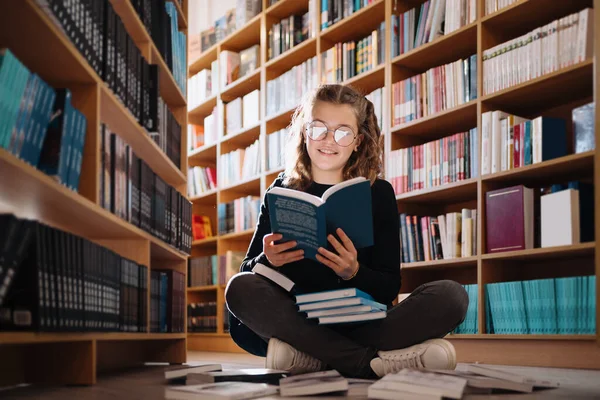 Όμορφη κοπέλα σπουδάζει διαβάζοντας ένα βιβλίο, ενώ κάθεται στο πάτωμα ανάμεσα στα βιβλία στο βιβλιοπωλείο — Φωτογραφία Αρχείου