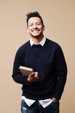 Siyah süveter ve gözlüklü, bej arka planda poz veren Afro yakışıklı bir adam.