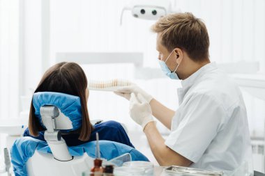Dişçi genç kadın dişlerinin rengini kontrol ediyor ve seçiyor
