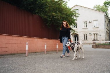 Yürüyen, tartışan ve şehirdeki dalmaçyalı evcil hayvanıyla oynayan bir kadın.