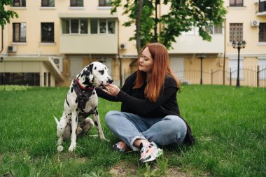 Güzel bir kadın sokak arka planında Dalmaçyalı köpeğe poz veriyor ve sarılıyor.