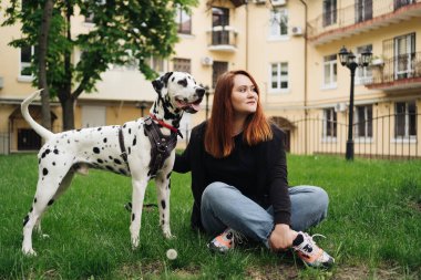 Güzel bir kadın sokak arka planında Dalmaçyalı köpeğe poz veriyor ve sarılıyor.