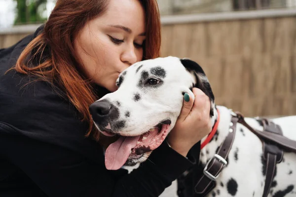 Sokak arka planında Dalmaçyalı köpeği öpen güzel bir kadın. — Stok fotoğraf