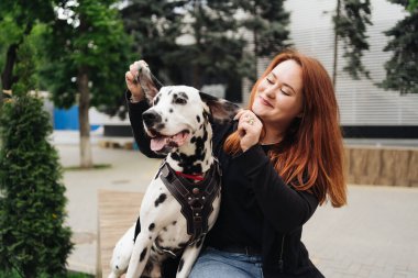 Güzel bir kadın sokak arka planında Dalmaçyalı köpeğe poz veriyor ve sarılıyor.