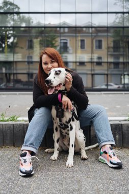 Güzel bir kadın sokak arka planında Dalmaçyalı köpeğe poz veriyor ve sarılıyor.