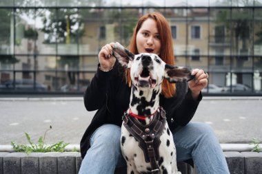 Güzel bir kadın sokak arka planında Dalmaçyalı köpeğe poz veriyor ve sarılıyor.