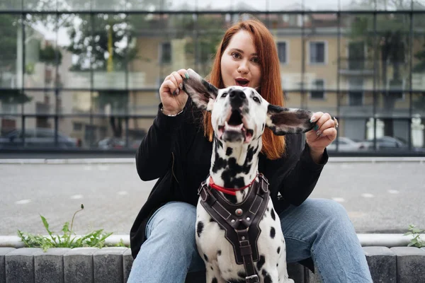 Όμορφη γυναίκα ποζάρουν και αγκαλιάζει dalmatian σκυλί στο δρόμο φόντο της πόλης — Φωτογραφία Αρχείου