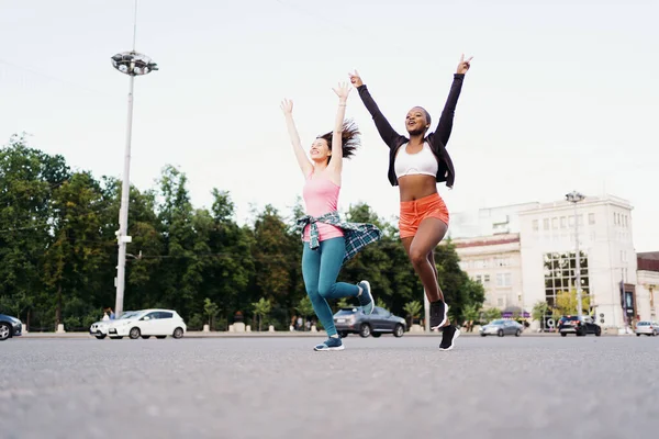 Zwei multiethnische Mädchen laufen durch die Straßen der Stadt und kommunizieren im Freien. — Stockfoto