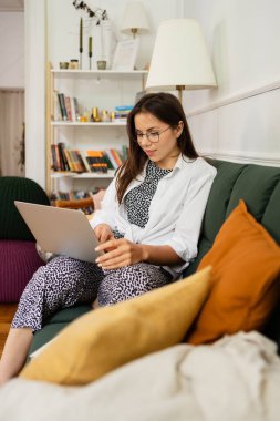 İş kadını dizüstü bilgisayarla çalışıyor evde oturuyor ve işlerini ev ofisinden yönetiyor.