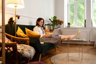 İş kadını dizüstü bilgisayarla çalışıyor evde oturuyor ve işlerini ev ofisinden yönetiyor.