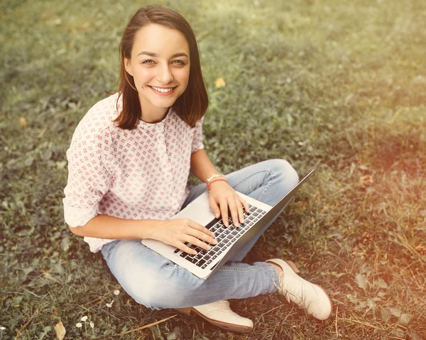 Young woman with laptop sitting on green grass — Stock Photo, Image