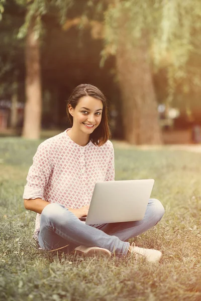 Giovane donna con computer portatile seduto su erba verde — Foto Stock