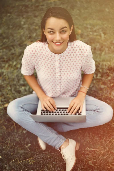 Jeune femme avec ordinateur portable assis sur l'herbe verte — Photo