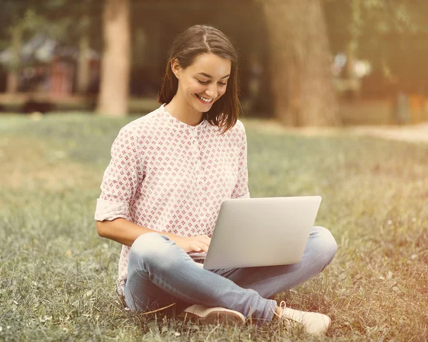 Giovane donna con computer portatile seduto su erba verde — Foto Stock